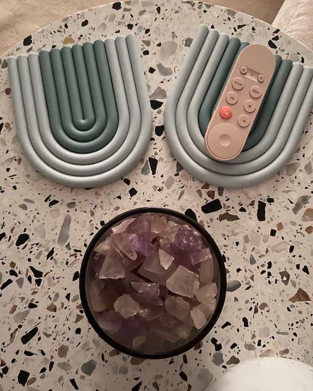 Textured stone tabletop with colourful stones in a bowl, google TV remote, and arch-shaped coasters