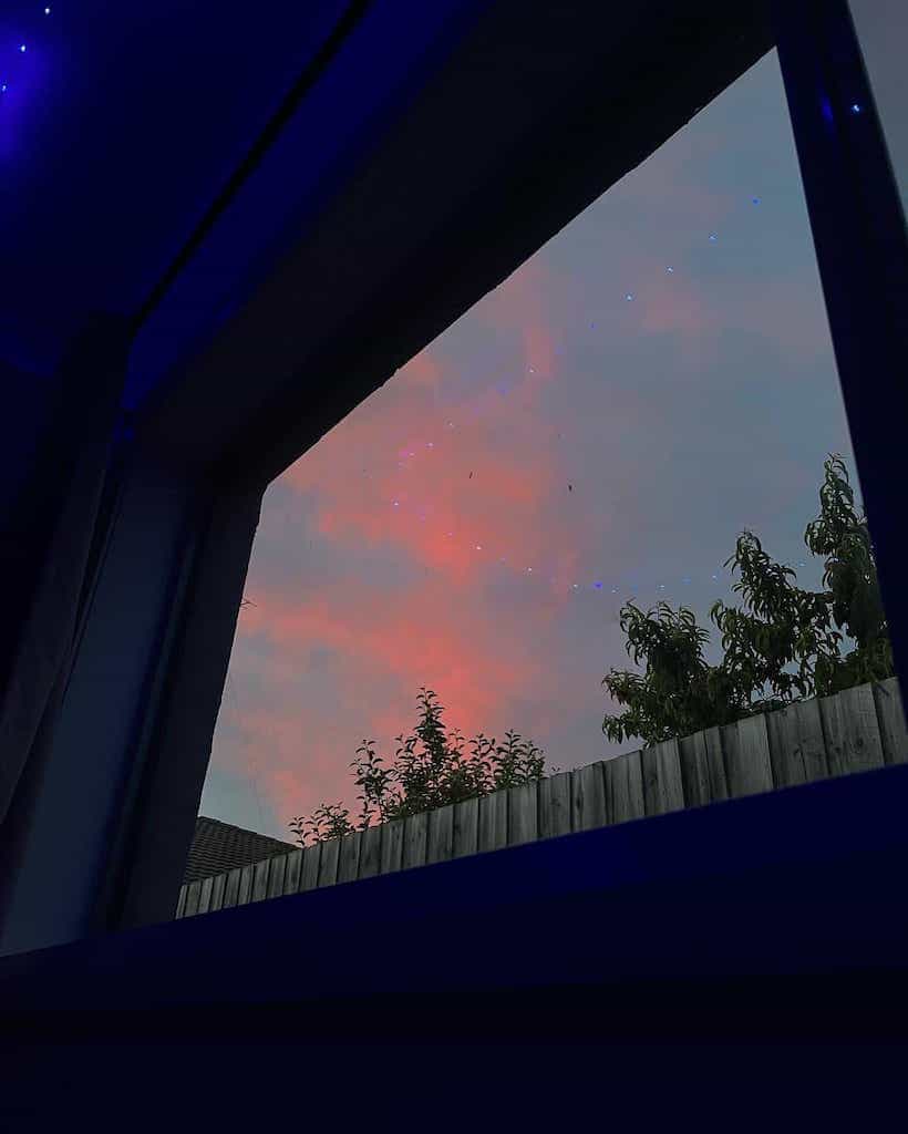 View out of window at sunset, dutch angle, inside is dark, blue hue, orange cloud visible in sky