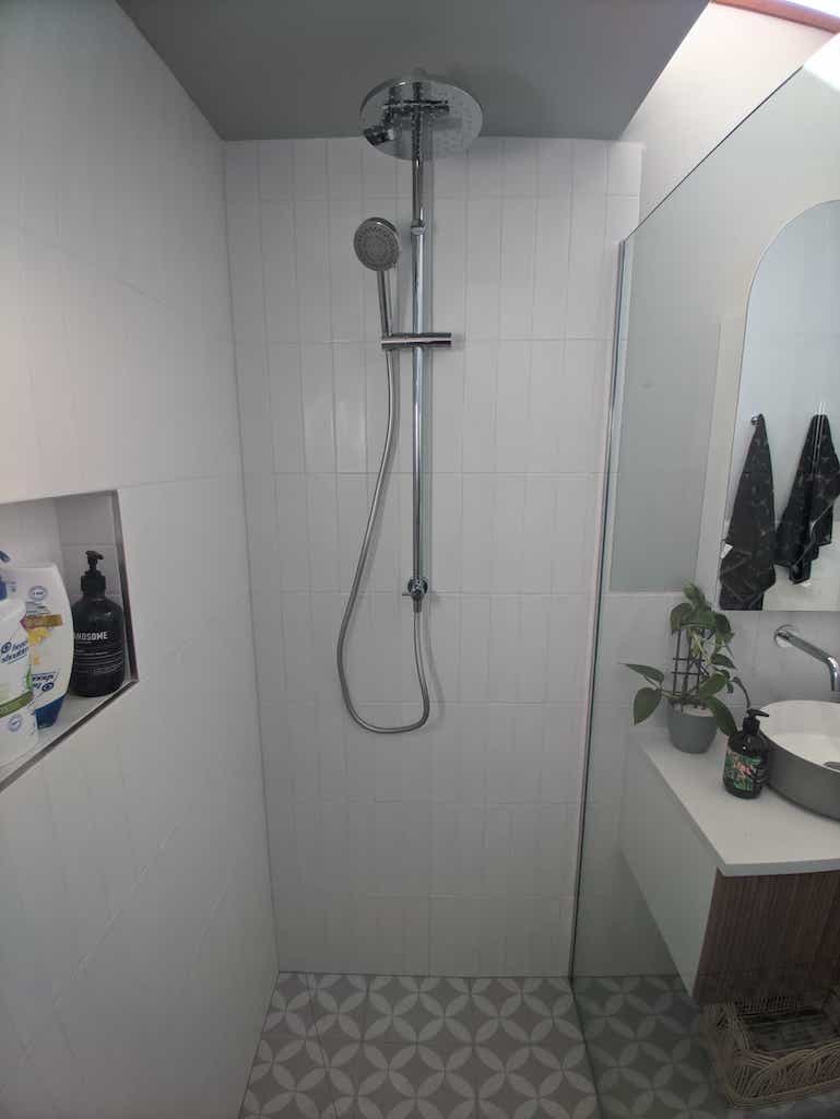 Image of shower, straight on, detachble shower head, glass divider on right, with niche on left